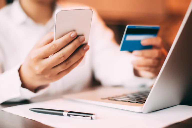 Person holding their phone and a credit card over a laptop